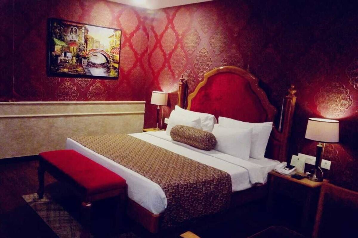 A hotel room with a large bed, a bench, two bedside tables with lamps, and a painting on the wall.