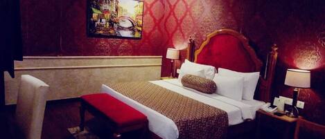A hotel room with a large bed, a bench, two bedside tables with lamps, and a painting on the wall.