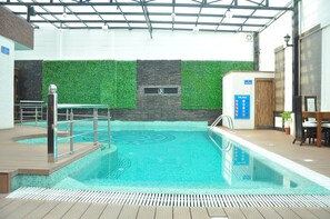An indoor swimming pool with a green wall and a wooden deck. - Hotel JSR Continental (Dehradun)