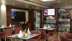 Een restaurant met gedekte tafels, een bar met flessenrekken en een scherm waarop een menu wordt getoond.