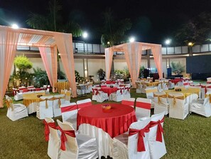 An outdoor event space with round tables and chairs, draped with white and red fabric.