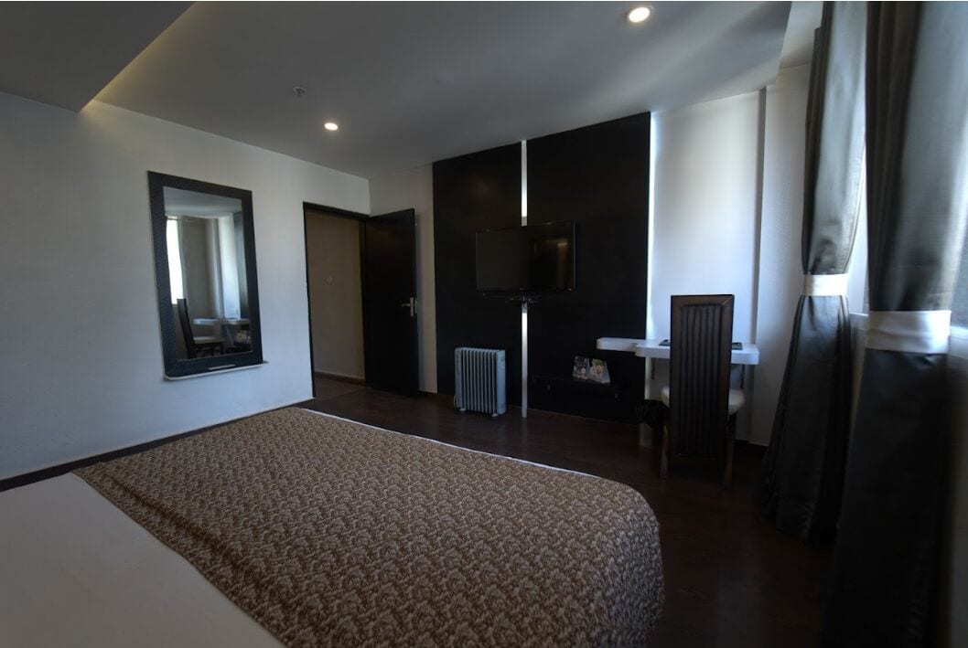 A hotel room with a large bed, a TV mounted on the wall, a desk, and a chair.