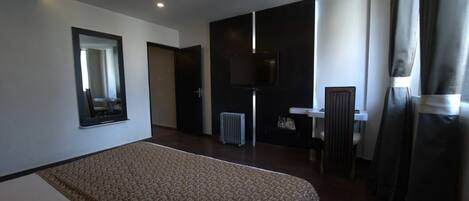 A hotel room with a large bed, a TV mounted on the wall, a desk, and a chair.