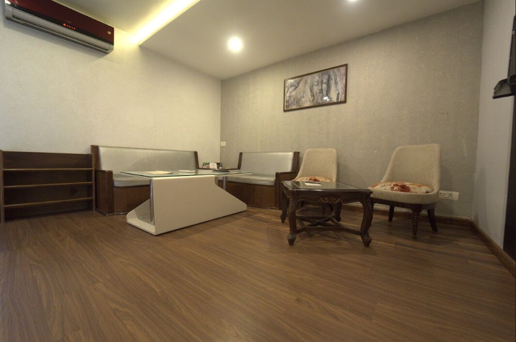 A hotel room with a bed, a desk, two chairs, a small table, and a wall-mounted air conditioner.