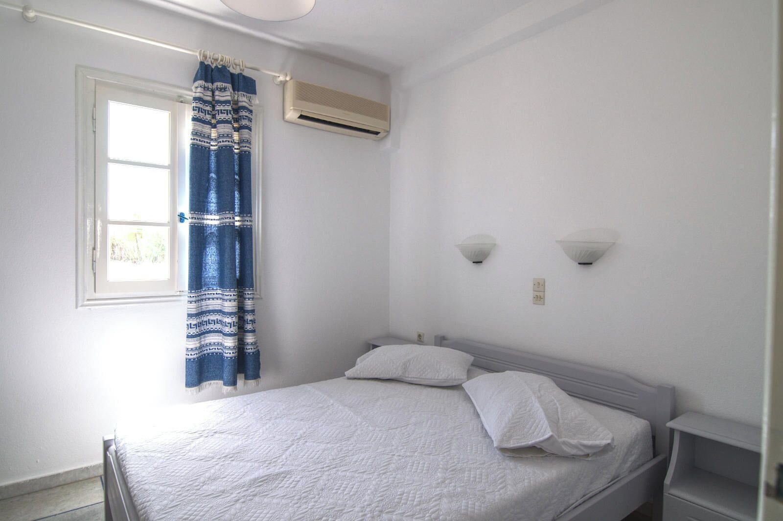 Ein Schlafzimmer mit Bett, einem Fenster mit Vorhang, einer Klimaanlage und zwei Wandleuchten.