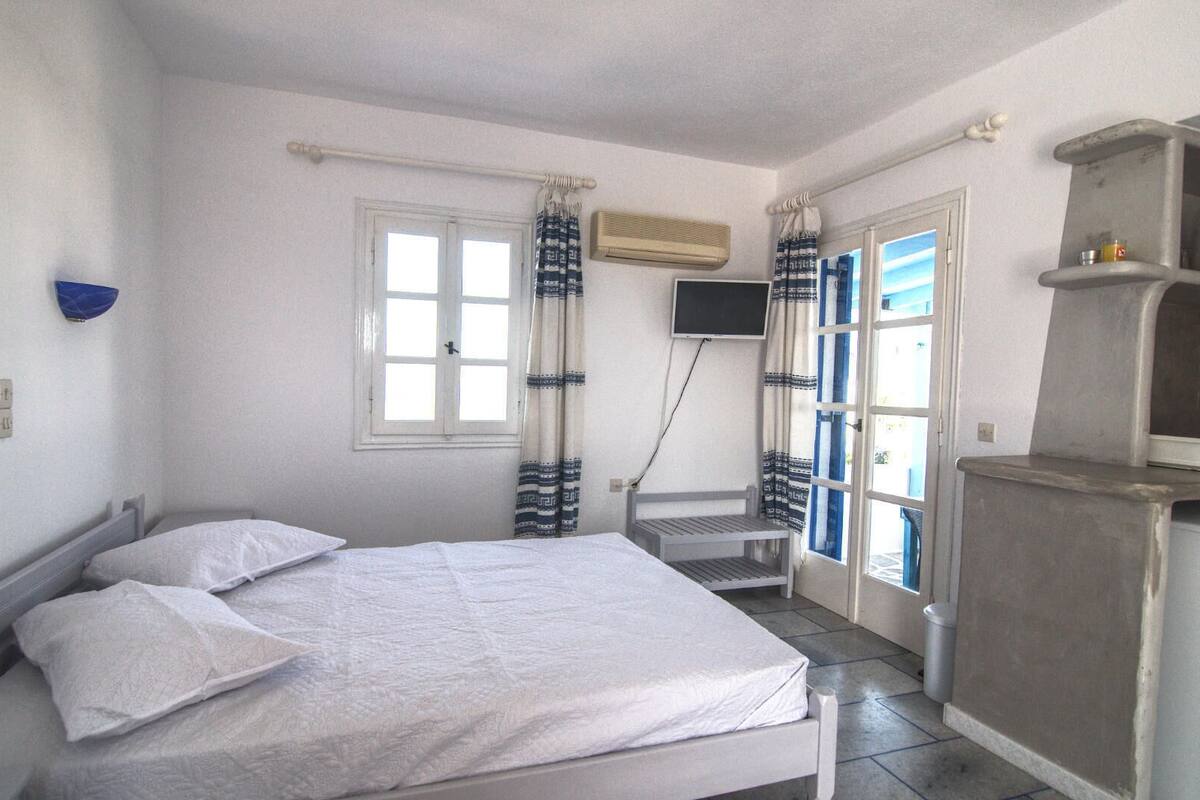 A bedroom with a bed, a TV, a window, and a shelf.
