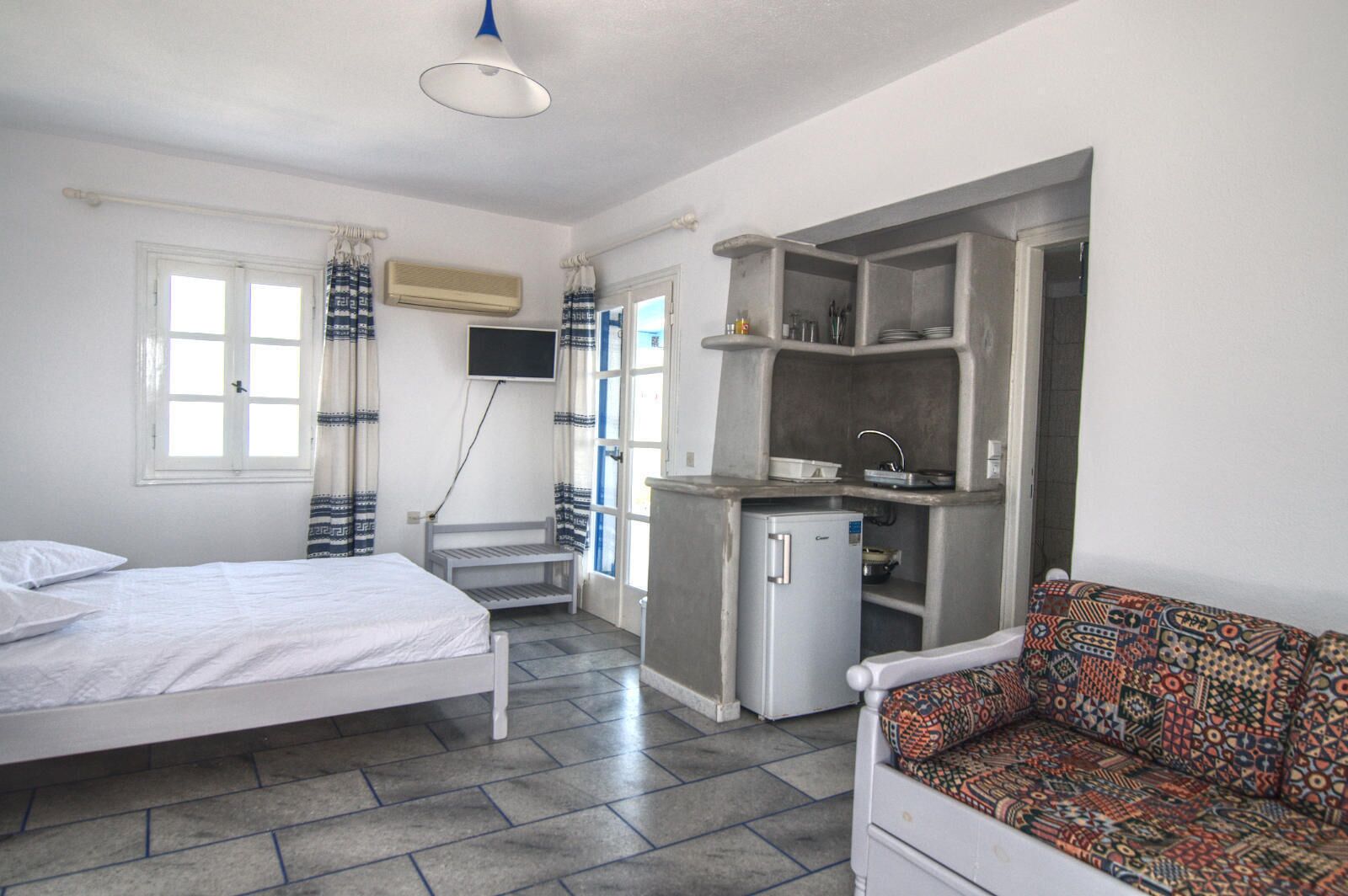 A compact room with a bed, a sofa, a kitchenette, and a TV.
