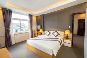 A hotel room with a large bed, two bedside tables with lamps, a window with curtains, and a view of buildings outside. - Navy Hotel Da Lat (Lam Vien - Da Lat)