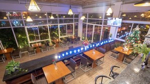 A restaurant with a long counter, multiple tables, and chairs. It has large windows with string lights and a Christmas tree. - Navy Hotel Da Lat (Lam Vien - Da Lat)