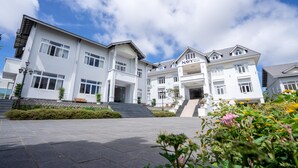 A multi-story hotel with a white exterior, multiple windows, and a sign reading "Navy Hotel." - Navy Hotel Da Lat (Lam Vien - Da Lat)