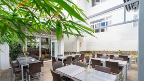 An outdoor dining area with multiple tables and chairs, surrounded by greenery and a stone wall. - Navy Hotel Da Lat (Lam Vien - Da Lat)