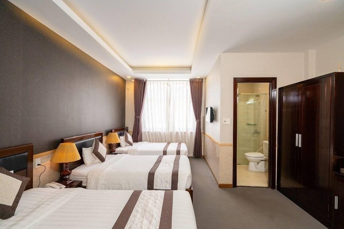 A hotel room with two beds, a wardrobe, a bathroom with a glass shower, and a TV.