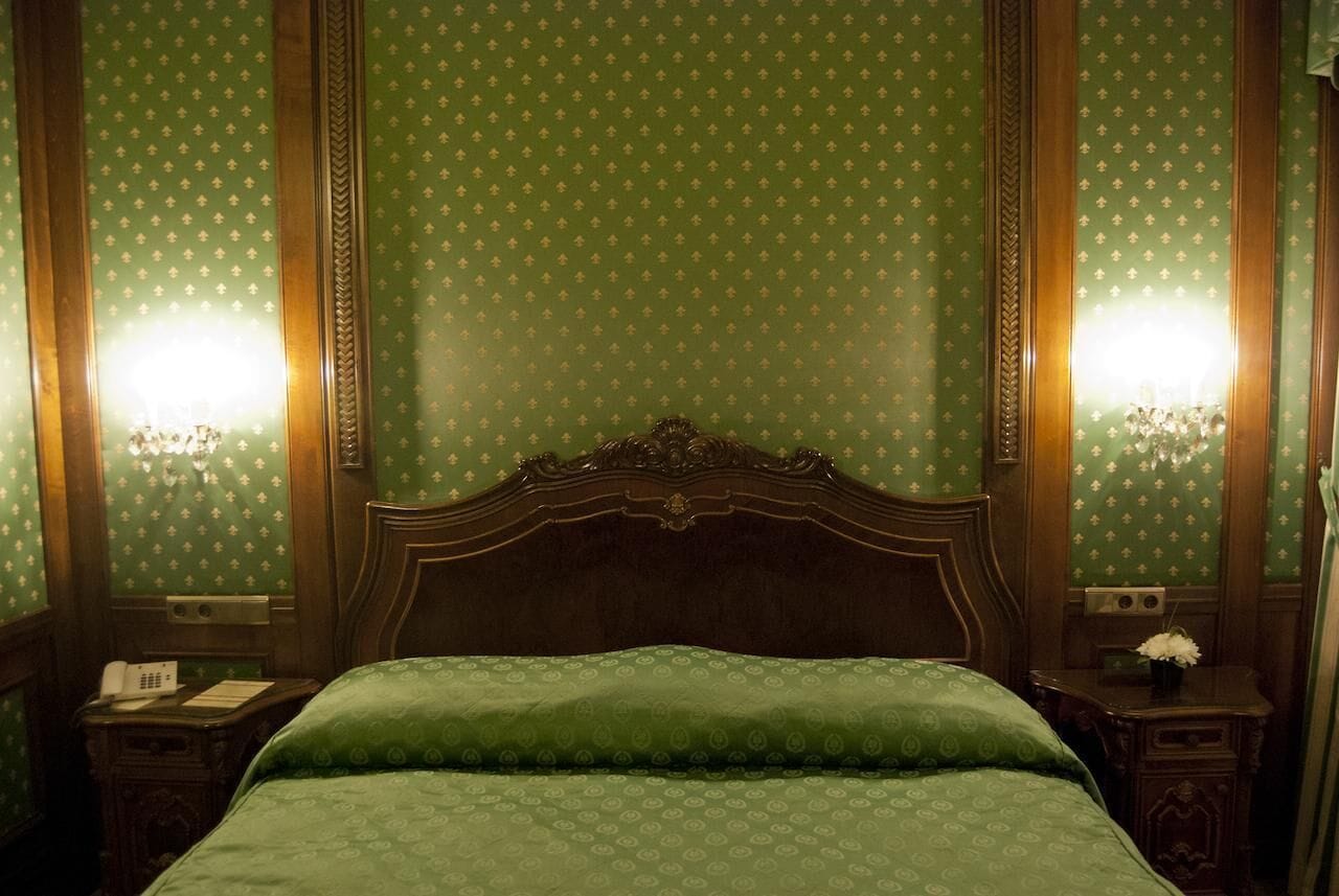 A room with a large bed, two bedside tables, a nightstand, and a wall-mounted telephone.
