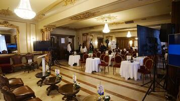 Ein prachtvoller Saal mit aufwendiger Deckenverzierungen, mehreren runden Tischen mit weißen Tischdecken und verschiedenen Sitzgelegenheiten, darunter Stühle und Sofas.