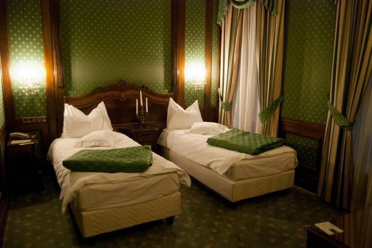 A hotel room with two beds, green patterned wallpaper, and curtains.
