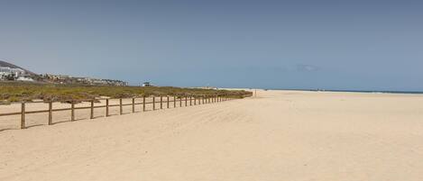 A wide sandy beach with a wooden fence running along the left side.