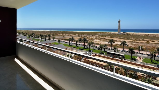 Een balkon met uitzicht op een strand, een vuurtoren en een weg met palmbomen.