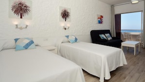 Een hotelkamer met twee bedden, een zwarte fauteuil, een klein tafeltje en uitzicht op zee.