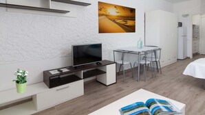 Une chambre moderne équipée d’un téléviseur à écran plat, d’une table à manger avec des chaises, d’un meuble blanc et d’un tableau accroché au mur.