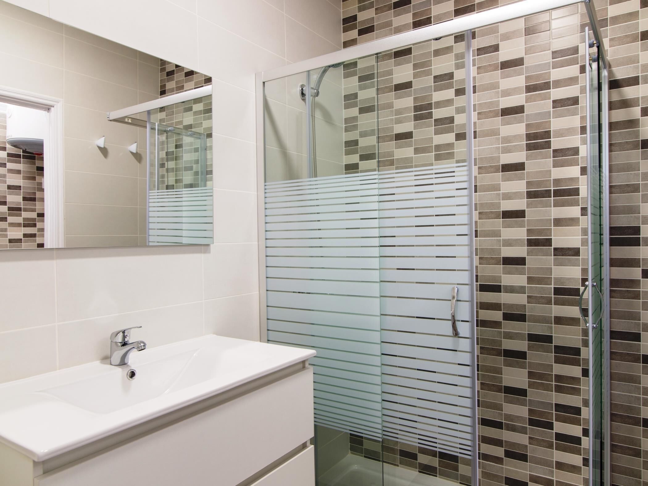 A bathroom with a glass-enclosed shower, a white sink, and a tiled wall with a mosaic pattern.