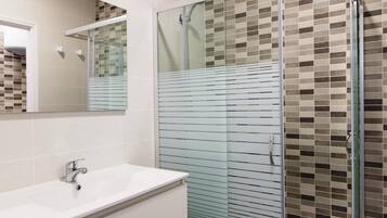 A bathroom with a glass-enclosed shower, a white sink, and a tiled wall with a mosaic pattern.