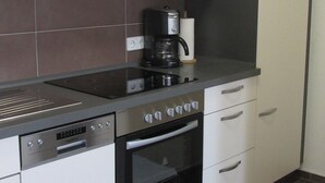 A modern kitchen with a stove, oven, dishwasher, and a coffee maker. - Ferienwohnung Neuenbau (Föritztal)