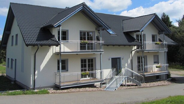 A two-story house with a sloped roof, multiple balconies, and a front entrance with a staircase. - Ferienwohnung Neuenbau (Föritztal)
