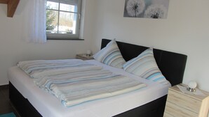 A bedroom with a bed, a nightstand, a window, and a wall-mounted artwork. - Ferienwohnung Neuenbau (Föritztal)
