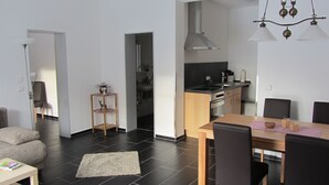 A modern kitchen with a central island, a dining area with a table and chairs, and a living space with a sofa and a rug. - Ferienwohnung Neuenbau (Föritztal)