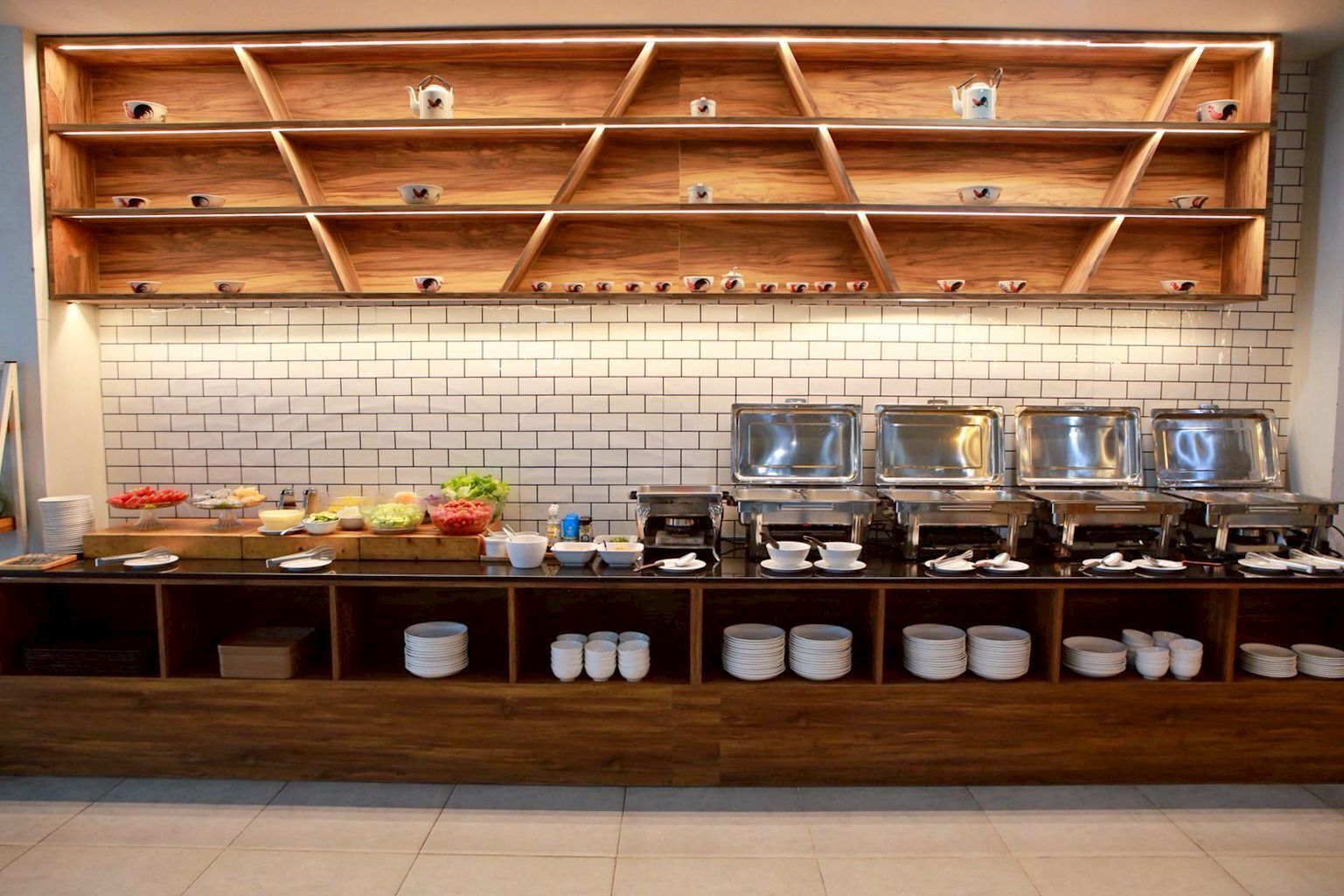 A buffet setup with multiple serving stations, a tiled backsplash, and wooden shelves above.