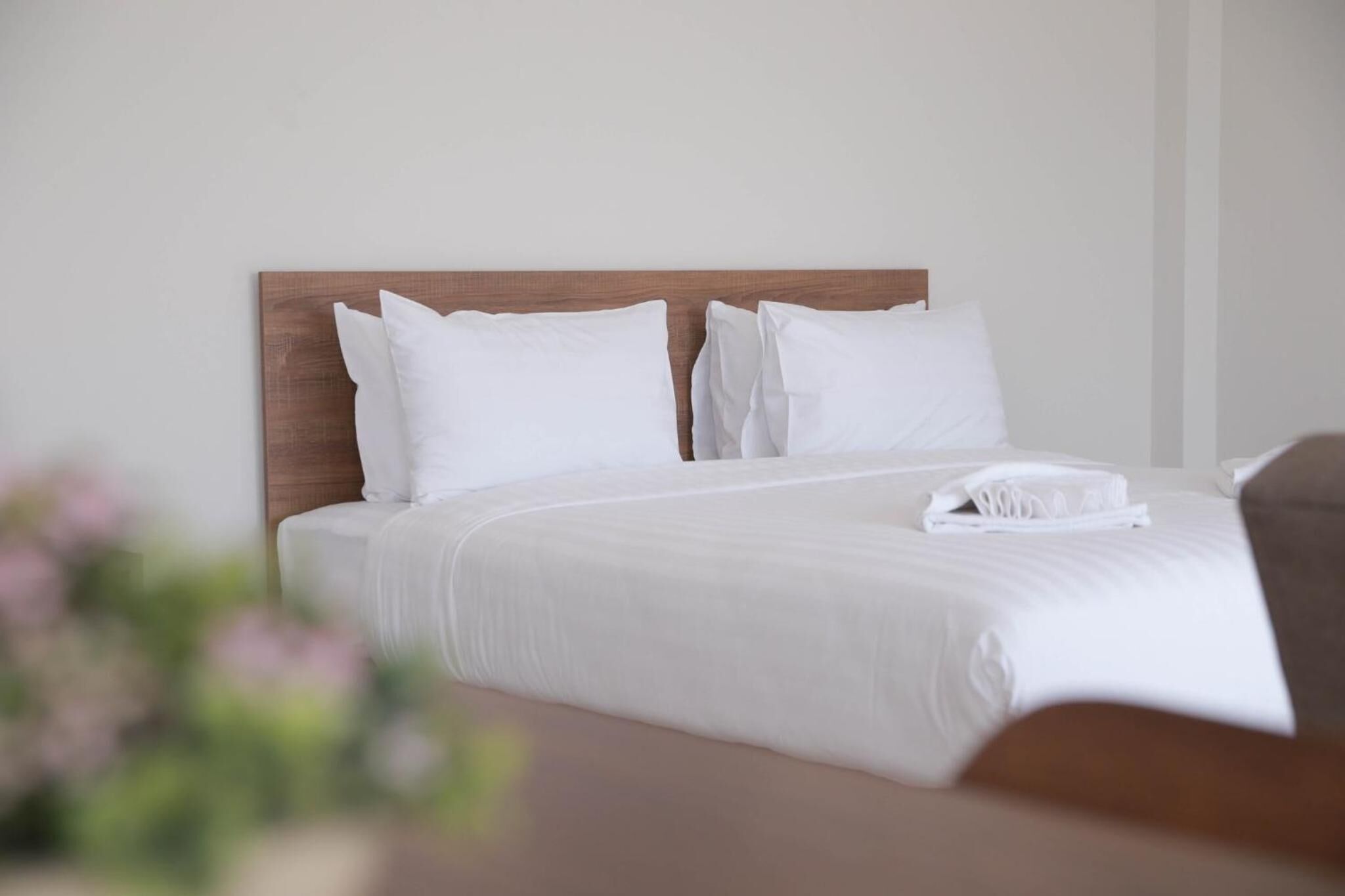 A neatly made bed with white linens and pillows, a wooden headboard, and a folded towel on the bed.