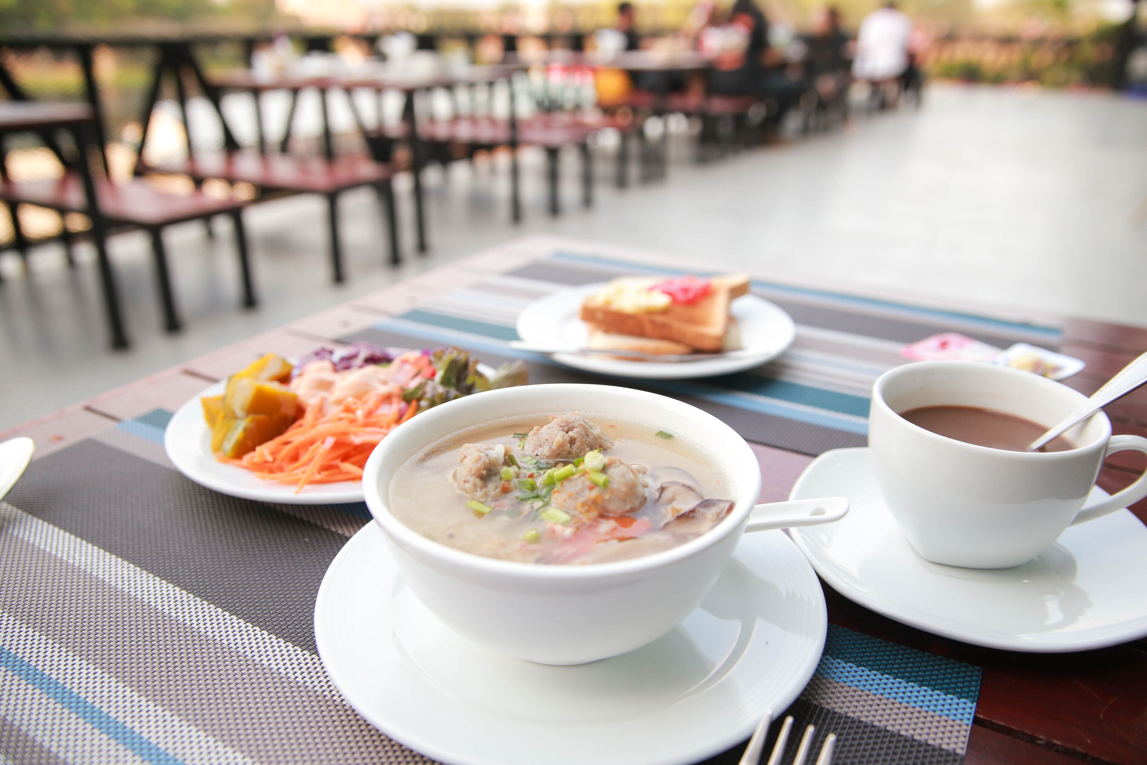 A dining table with a bowl of soup, a cup of coffee, and a plate of food.