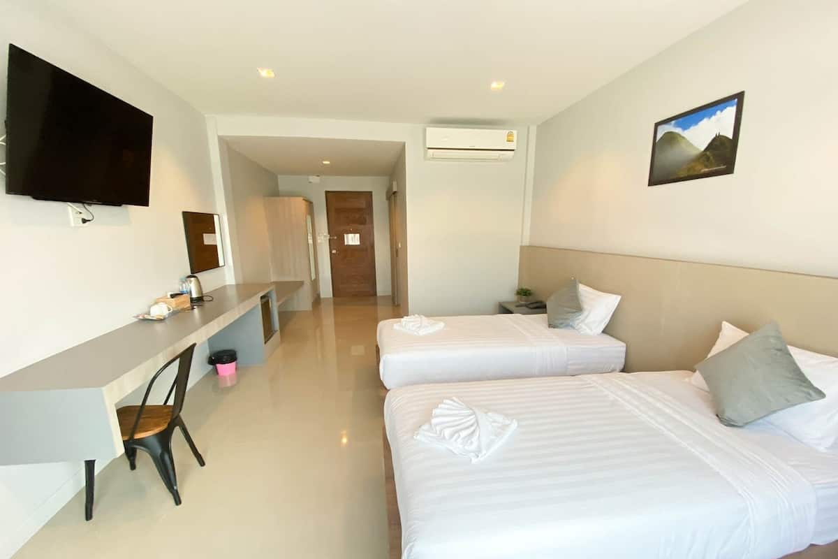 A hotel room with two beds, a desk, a chair, a flat-screen TV, and an air conditioning unit.