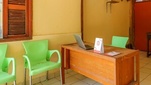 A wooden desk with a laptop and a brochure, flanked by two green chairs in a room with yellow walls and a window with blinds. - OYO 1755 De'balcon Accomodation Near Ngurah Rai Airport (Kuta)