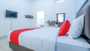 A modern hotel room with a large bed, a flat-screen TV mounted on the wall, a small desk with a mirror, and a window providing natural light. - OYO 1755 De'balcon Accomodation Near Ngurah Rai Airport (Kuta)