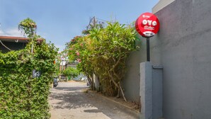 A narrow street with a red sign on a wall, a parked car, and greenery. - OYO 1755 De'balcon Accomodation Near Ngurah Rai Airport (Kuta)