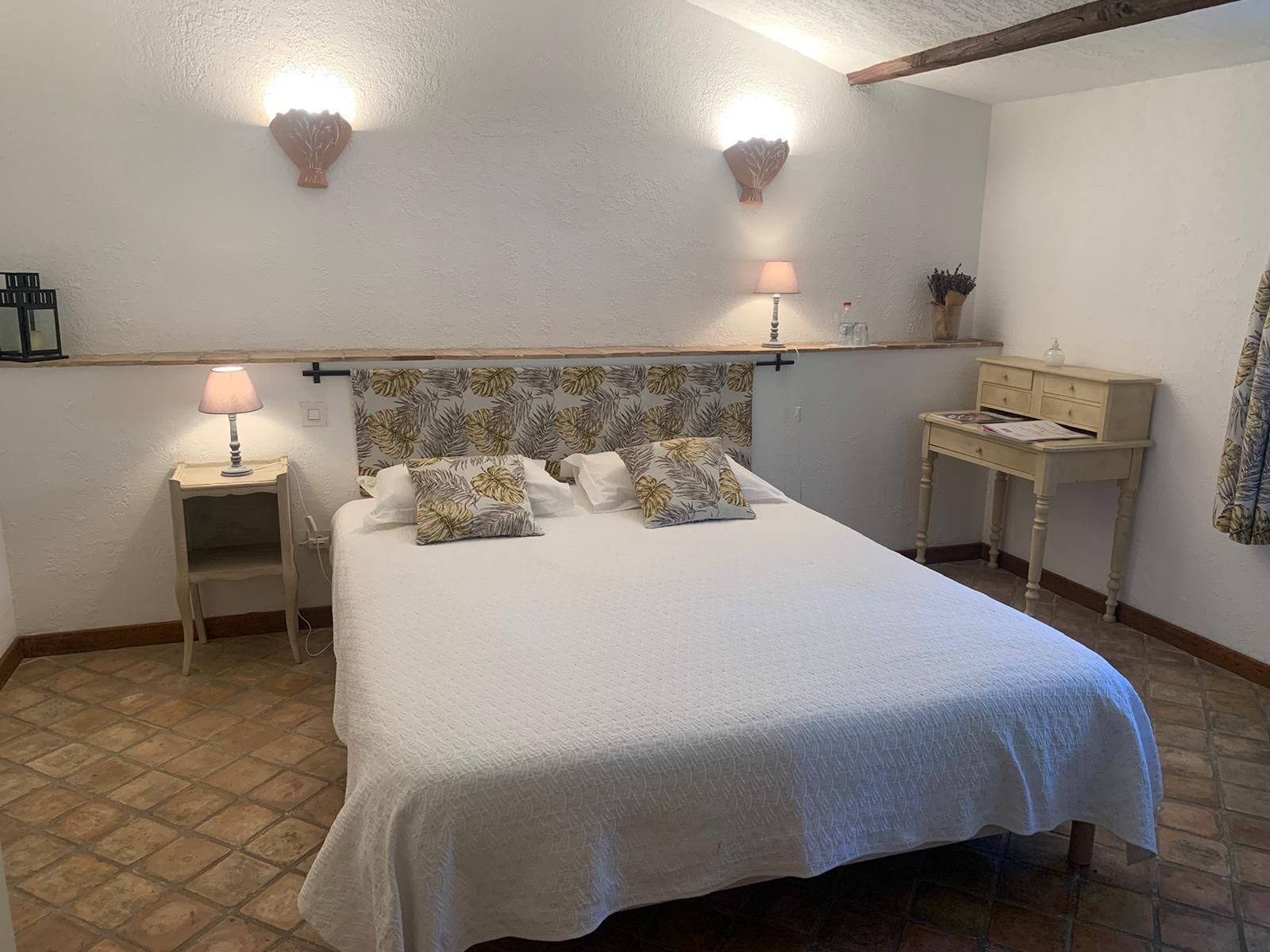 Una cama bien hecha con un cabecero floral, dos lámparas de noche y una mesita auxiliar.