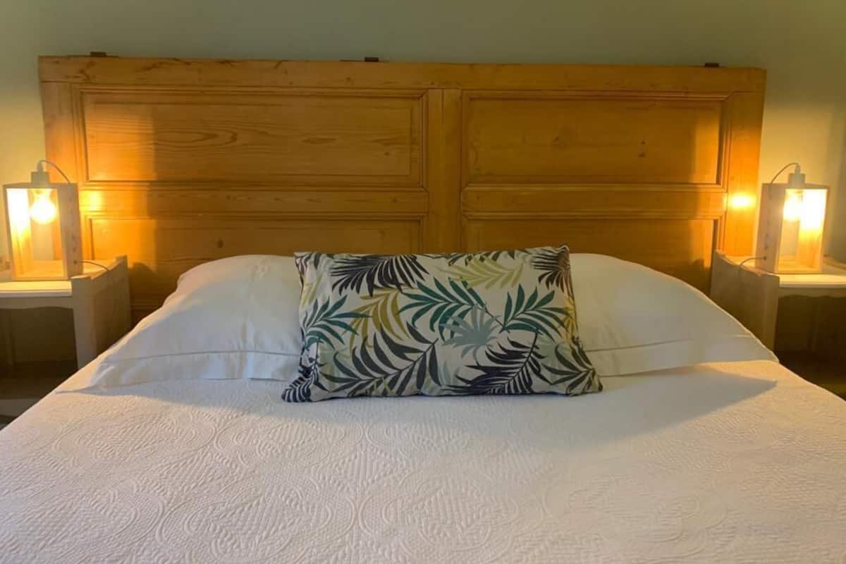 A bed with a white bedspread and a leaf-patterned pillow, flanked by two nightstands with lamps.