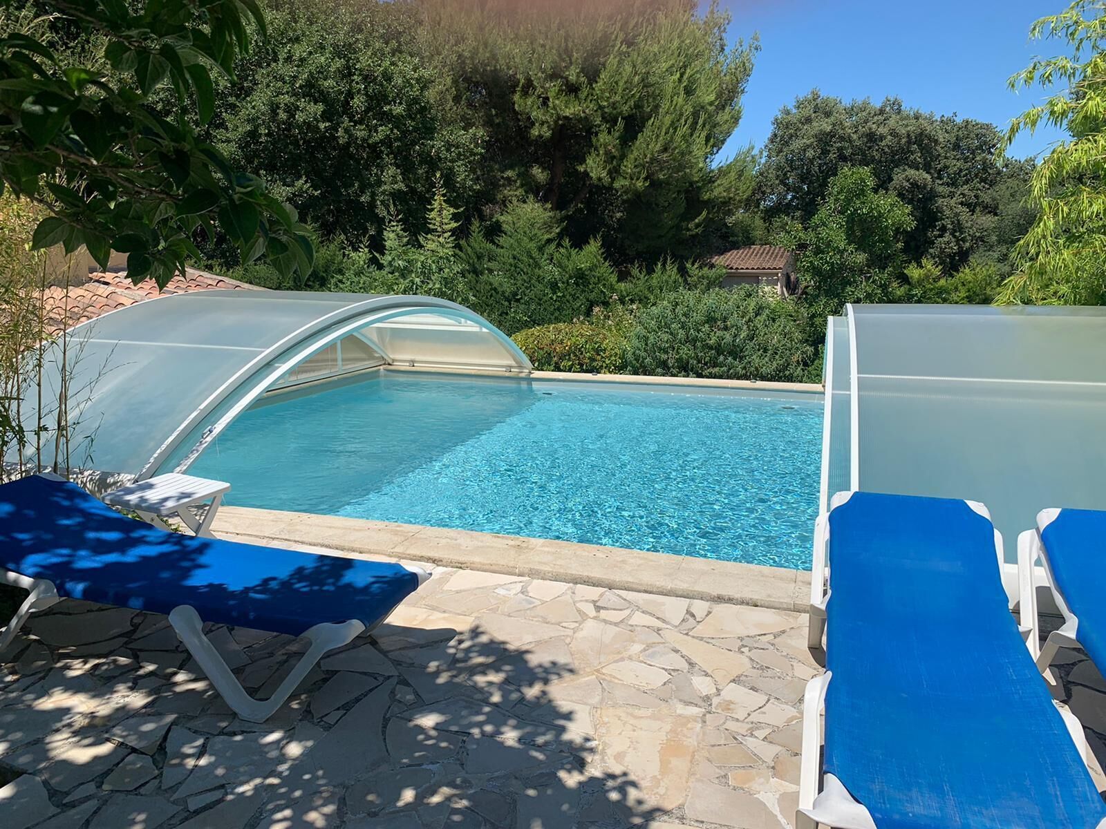 A swimming pool with a glass enclosure, surrounded by stone tiles and blue lounge chairs.