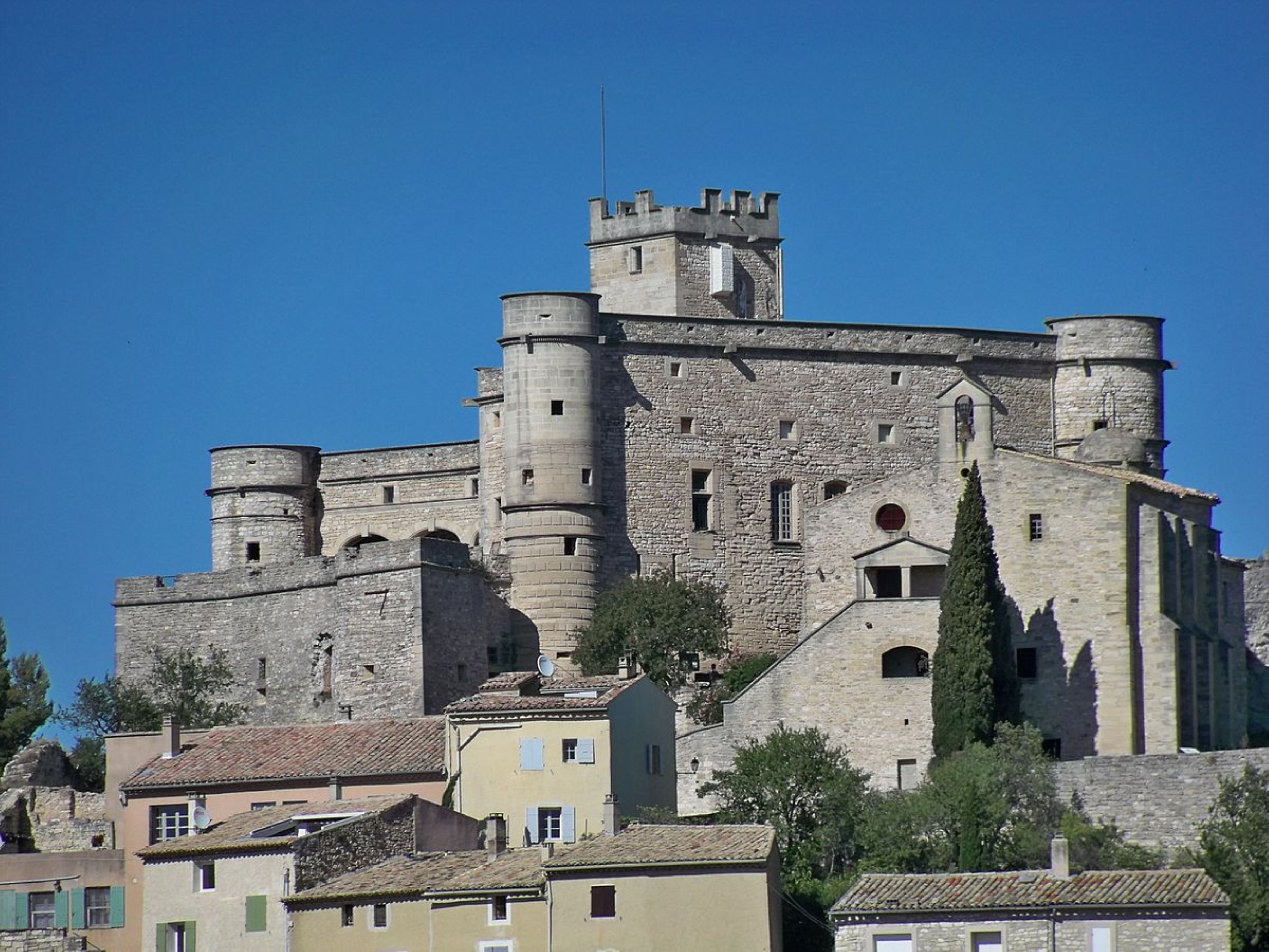 A historic stone castle with multiple towers and a fortified wall, surrounded by traditional buildings.