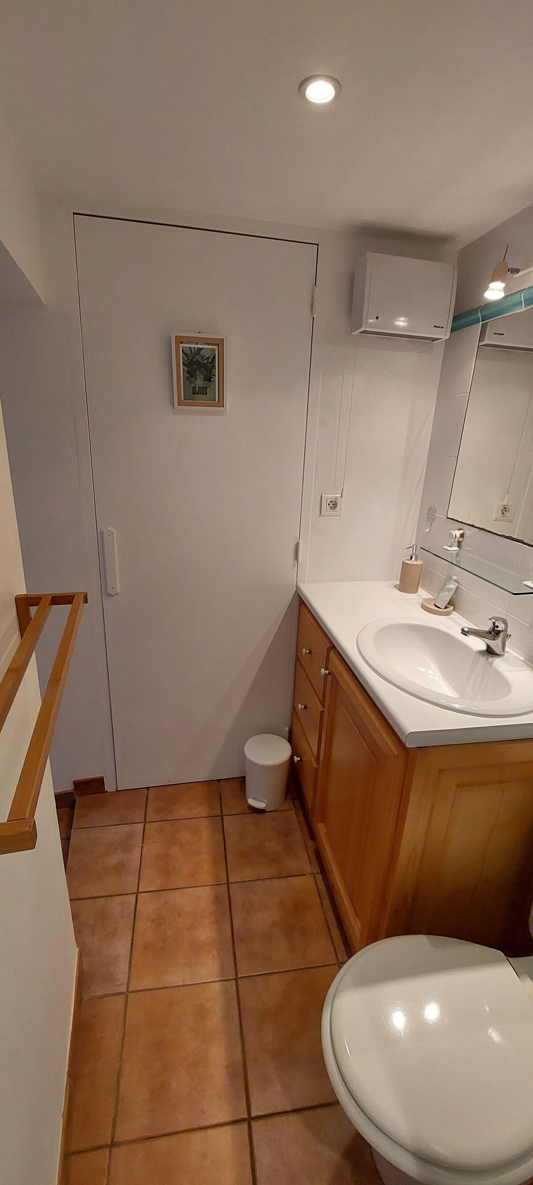 Une salle de bain avec un lavabo blanc, un meuble en bois et un petit tableau encadré accroché au mur.