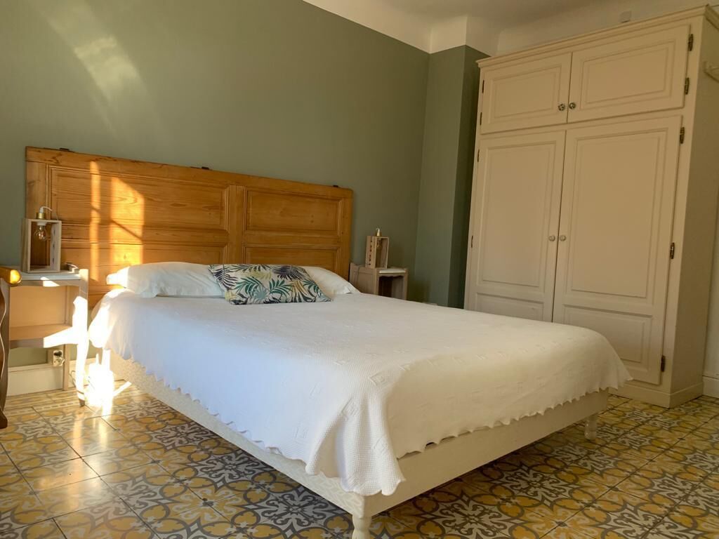 Un dormitorio con cabecera de madera, cama con ropa blanca, mesita de noche con lámpara y armario.