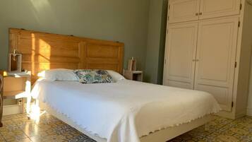 Un dormitorio con cabecera de madera, cama con ropa blanca, mesita de noche con lámpara y armario.