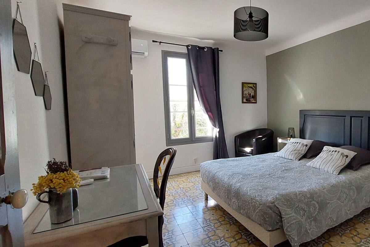 A bedroom with a bed, bedside table, chair, and a window with curtains.