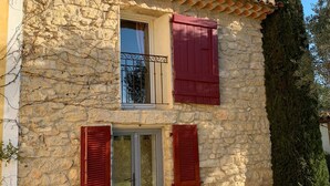 A stone building with a tiled roof, red shutters, and a small window with a metal gate. - Bastide Sainte Agnes (Carpentras)