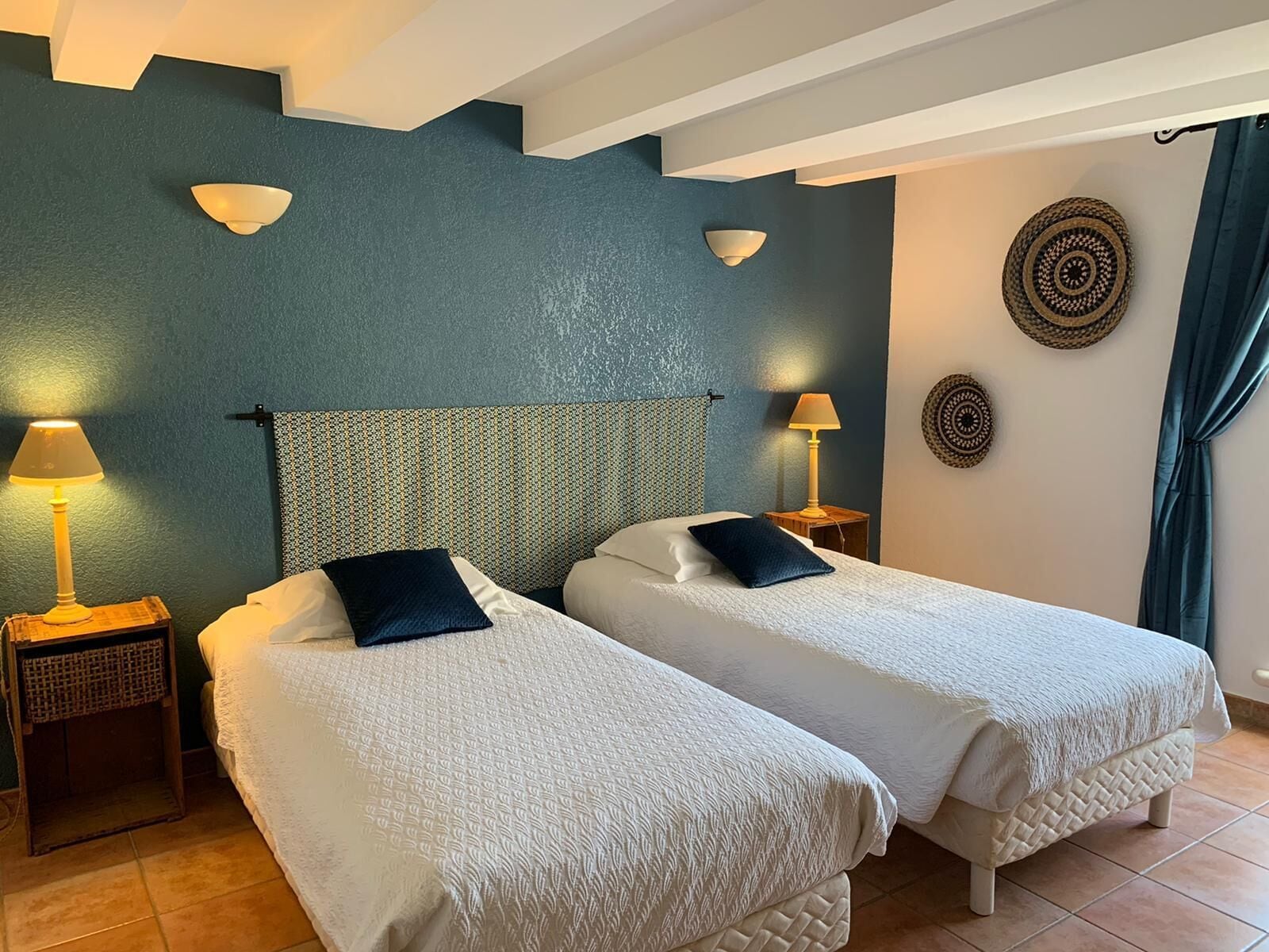 Een hotelkamer met twee bedden, een gestreept hoofdbord, wandlampen en een wanddecoratie van geweven materiaal.
