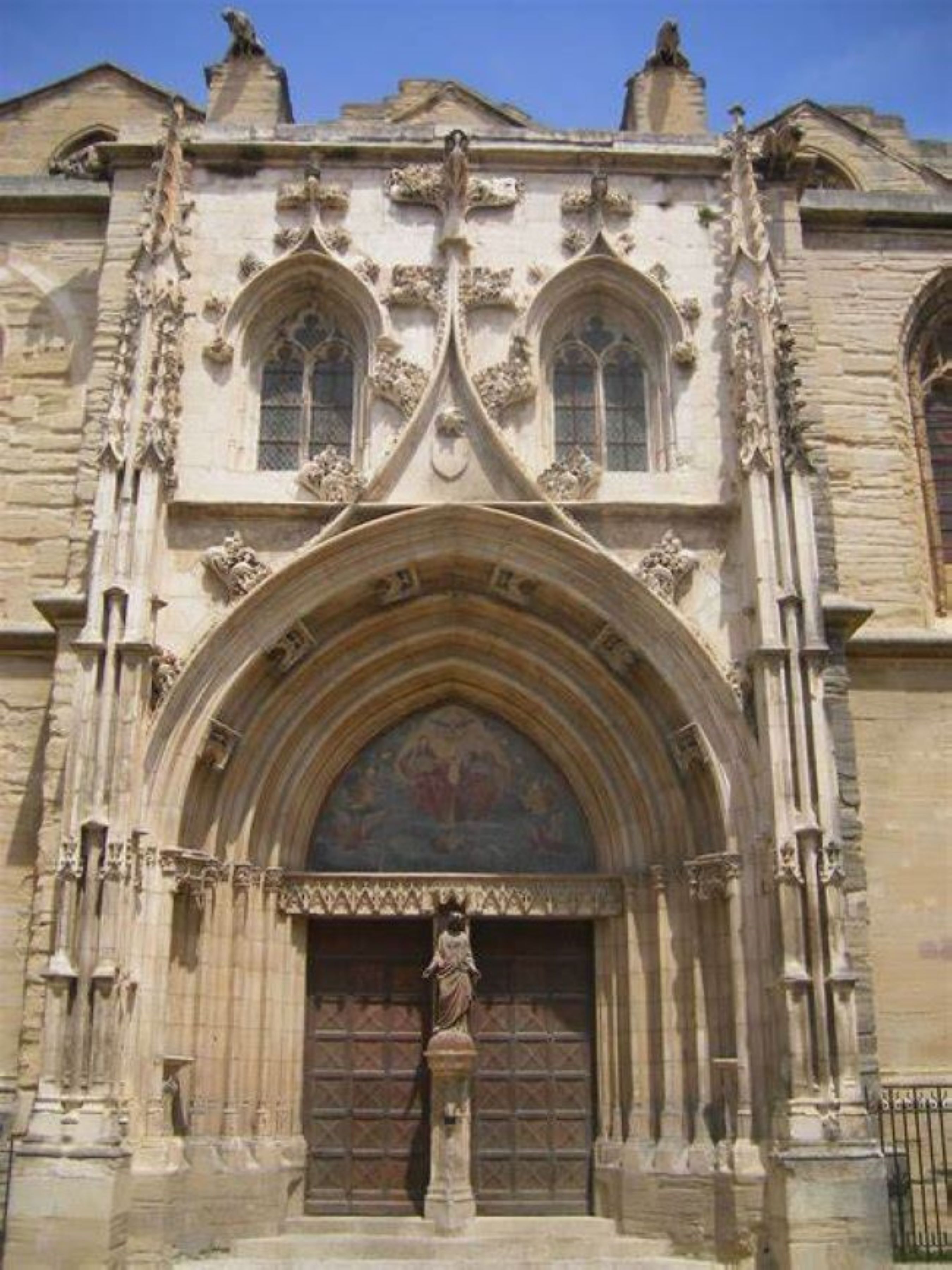 Un bâtiment historique doté d’une grande entrée en arc de cercle, de sculptures en pierre détaillées et d’une statue à sa base.