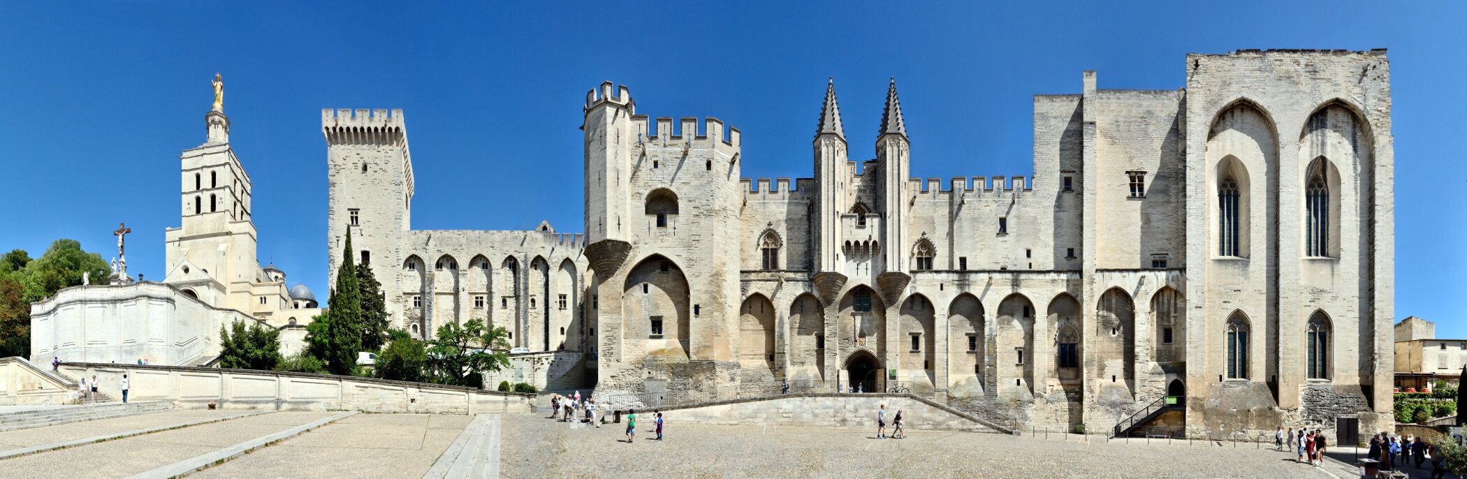 A historic castle with multiple towers and arched windows, a large courtyard, and a statue on a pedestal.