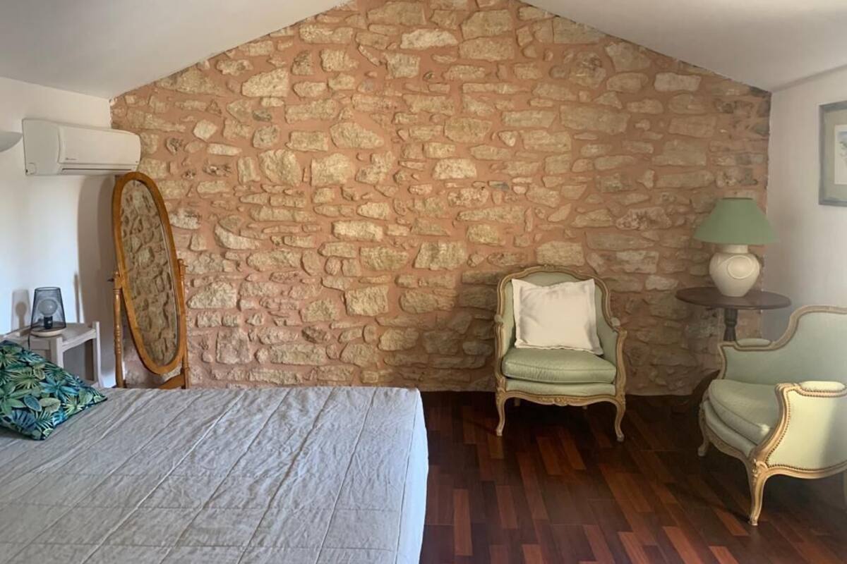 A bedroom with a stone wall, a bed, a chair, and a lamp.