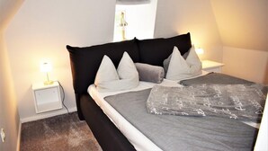 Une chambre à coucher avec une tête de lit noire, des oreillers blancs, une couverture grise et une lampe de chevet.